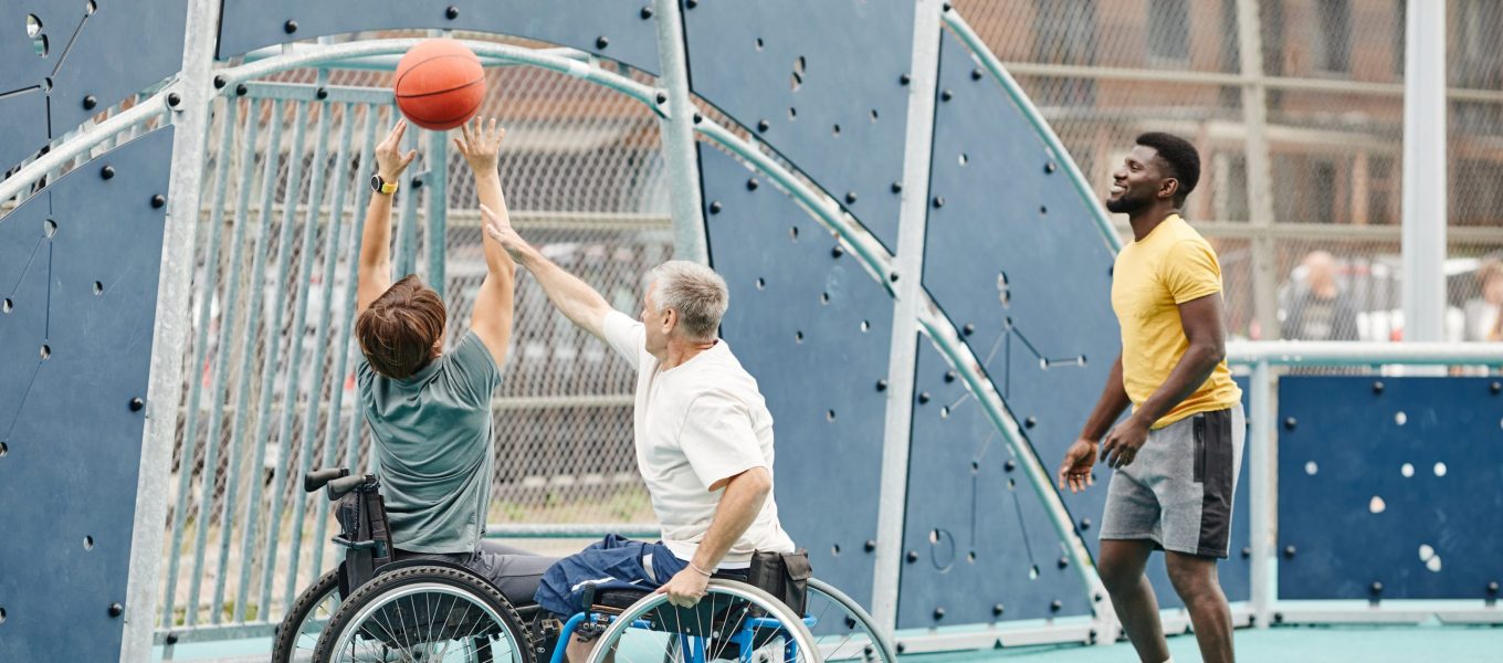 African sportsman playing basketball outdoors together with couple with disability